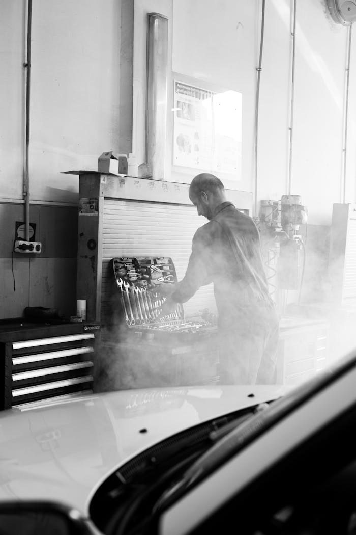 Offerings Mechanic in a garage performing vehicle maintenance amidst tools and equipment in a smokey atmosphere.